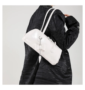 Detail of white glossy shoulder bag with bow decor and heart chain on black jacket