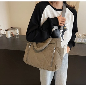 Detail view of khaki quilted shoulder bag with white topstitching and dual front zippers