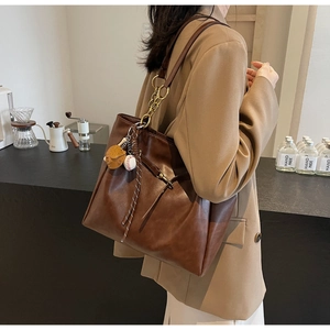 Detail view of brown leather tote bag with chain strap and baseball theme pendant