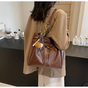 Detail of dark brown leather tote bag with gold chain strap and baseball charm accessory