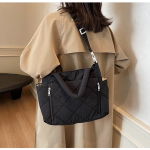Detailed back view of a black quilted shoulder bag worn with a khaki trench coat