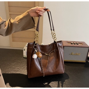 Detail of dark brown faux leather tote bag with chain strap and baseball glove charm
