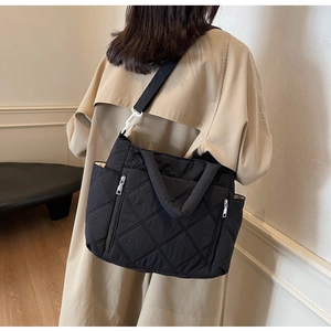 Detail of black quilted shoulder bag featuring side zipper and white buckle attachment
