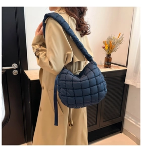 Detail view of a large navy blue quilted puffer tote bag worn over a khaki trench coat