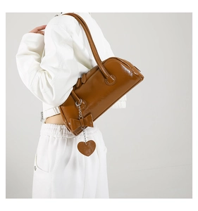Close-up of caramel brown leather shoulder bag with metallic heart charm and bow detail