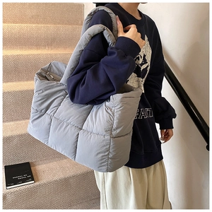 Close-up of gray quilted puffer tote bag with wide shoulder strap on model's shoulder