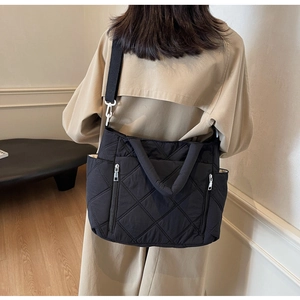 Rear view of a model wearing a black quilted nylon tote bag with wide crossbody strap
