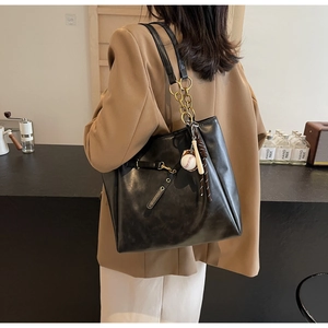 Detail of black PU leather tote with gold chain strap and baseball charm in lifestyle setting