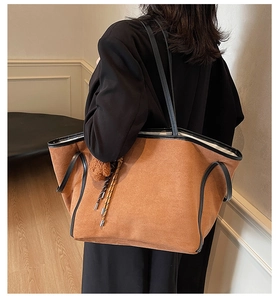 Detail of large brown suede tote bag with black trim and plush pompom charm shown on shoulder