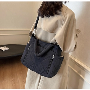 Detail view of black quilted tote bag with side zipper and white buckle on shoulder strap