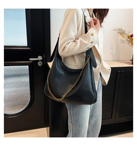Detail of a large black PU leather shoulder bag with a fine gold chain on a white blazer outfit