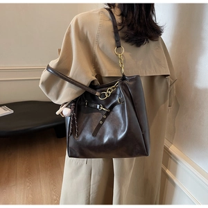 Detail of dark brown faux leather tote bag with gold chain and baseball charm accessory