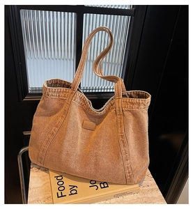Detailed view of brown denim tote bag showing leather brand logo and fabric texture