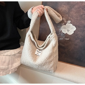 Close-up of beige plush tote bag texture with a Muheti logo patch and soft faux fur material