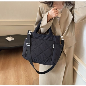 Detail of black quilted nylon bag with white buckle on model in beige trench coat