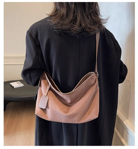 Détail d'un sac cabas en daim marron avec bandoulière réglable et étiquette décorative