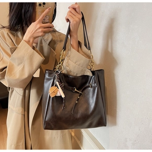 Detail view of deep brown PU tote bag with gold chain strap and baseball charm accessories