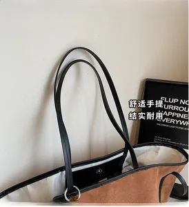 Detail of a brown suede tote bag with black leather handles and magnetic clasp