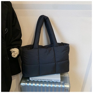 Minimalist black quilted puffer tote bag with padded handles on a silver suitcase