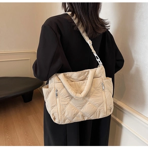 Detail of beige quilted tote bag with side pockets shown on model in a minimalist room