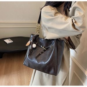 Detail of dark brown leather tote with gold chain strap and decorative charms on a model