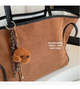 Close-up of brown suede tote bag featuring black leather trim and a cute plush dog pendant