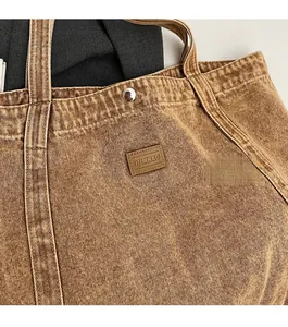 Detail of vintage brown denim fabric tote with leather brand tag and metal snap button