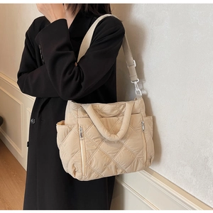 Detail showing the beige quilted fabric texture and functional zipper pocket on tote bag
