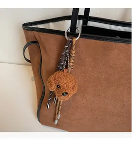 Detailed view of a brown plush poodle charm attached to a suede tote bag handle