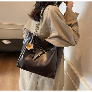 Detail view of large brown faux leather tote bag with metal chain strap and mushroom charm