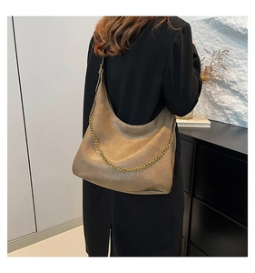 Detail of khaki PU leather shoulder bag with gold chain strap on a model indoors