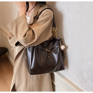 Detail of dark brown leather tote bag with gold chain strap and baseball charm on coat