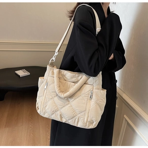Detail of cream quilted nylon tote with side zipper pockets on a black coat model