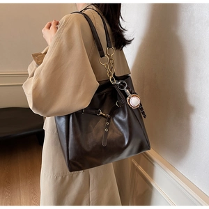 Detail of dark brown leather tote bag with gold chain strap and baseball charm
