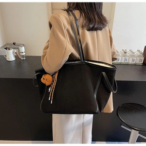 Detail view of large black PU leather tote bag with cute plush bear charm on shoulder