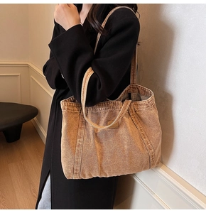 Detailed close-up of brown washed denim tote bag with vintage texture and metal logo tag