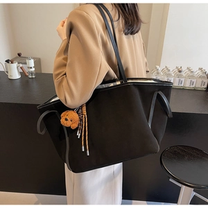Detail of a large black tote bag with plush bear charm and slender straps on a model