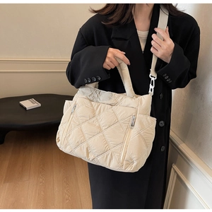 Close-up of cream quilted shoulder bag with classic diamond stitching and wide fabric strap