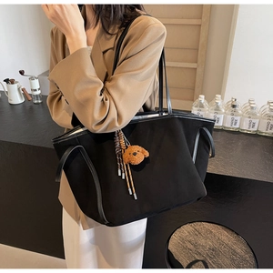 Close-up of black PU tote bag with a cute brown plush bear charm and woven tassel detail