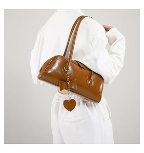 Detail of glossy brown oil-wax leather shoulder bag with chic bow and heart pendant