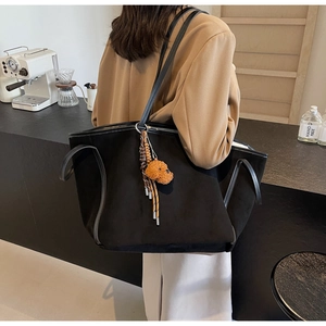 Close-up of black suede tote bag with woven strap and cute plush puppy charm detail