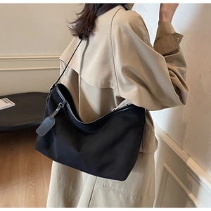 Sac à bandoulière demi-lune noir porté par un mannequin en trench-coat beige