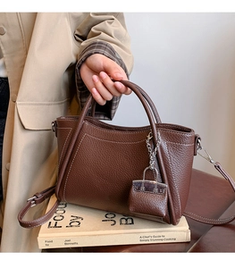 Detailed macro view of dark brown litchi pattern PU leather handbag with white contrast stitching