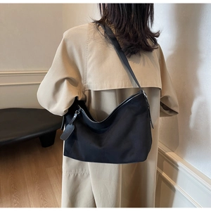 Vue latérale d'un sac hobo en croissant noir porté à l'épaule avec un trench-coat beige chic