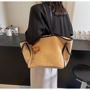 Detail of khaki suede tote bag with black leather straps and a cute brown bear charm