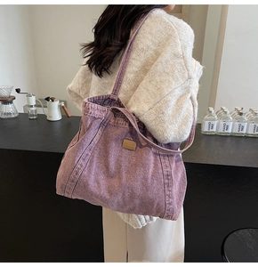 Detail of a purple canvas tote bag featuring a leather logo patch and drawstring closure