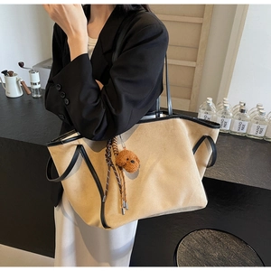 Detail of a large khaki suede tote bag with black leather trim and cute bear charm