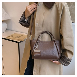Detail view of coffee PU leather handbag with white contrast stitching and mini pouch charm