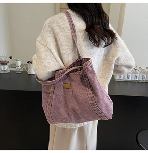 Detail of purple washed canvas tote bag with leather logo patch shown in a cafe setting