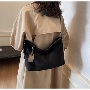 Sac hobo noir minimaliste porté par un mannequin avec un trench-coat kaki pour le bureau